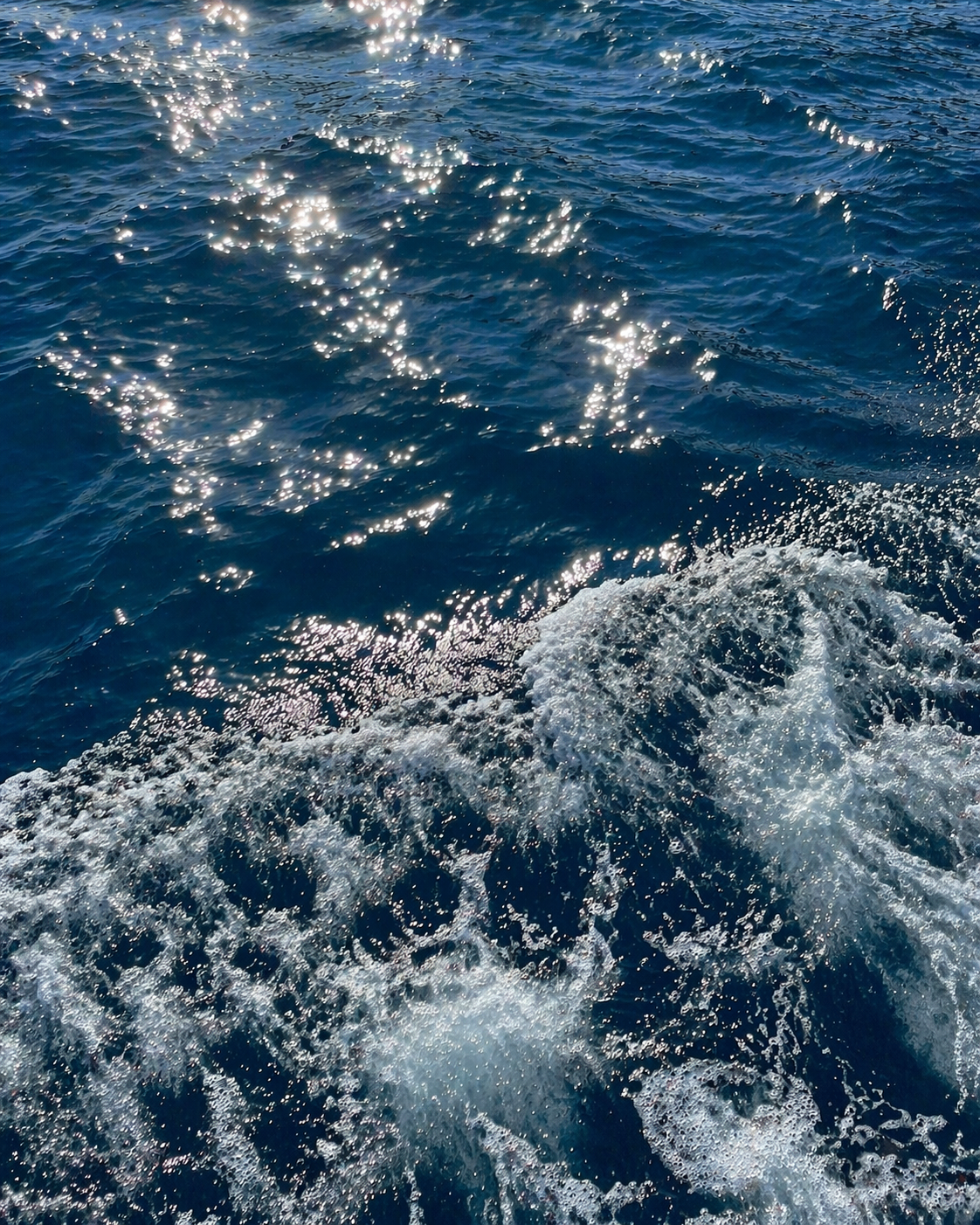 Sillage d'un bateau sur une mer bleu profond, éclats de lumière sur l'eau